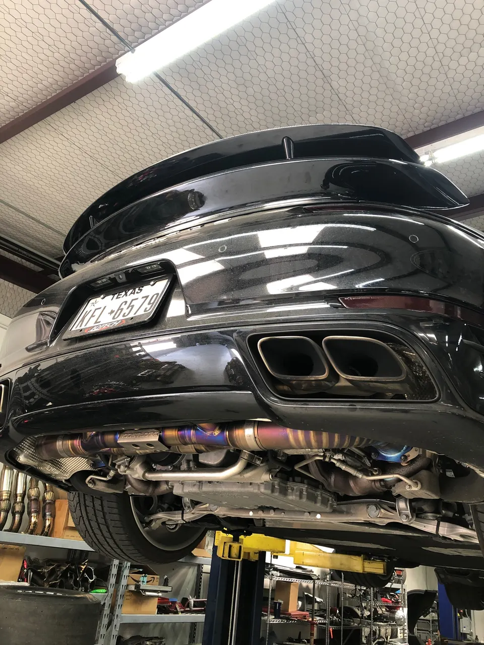 A Porsche on a lift in a shop, showcasing its aftermarket titanium exhaust system and underbody components.