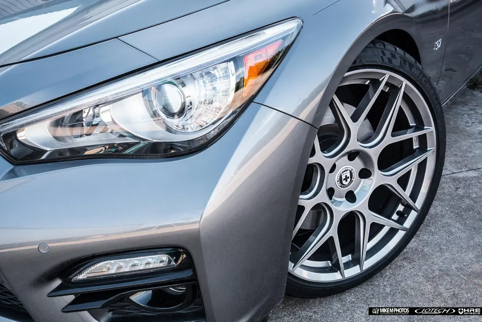 A grey Infiniti Q50 with custom HRE wheels, showcasing the front headlight and fender in detail.