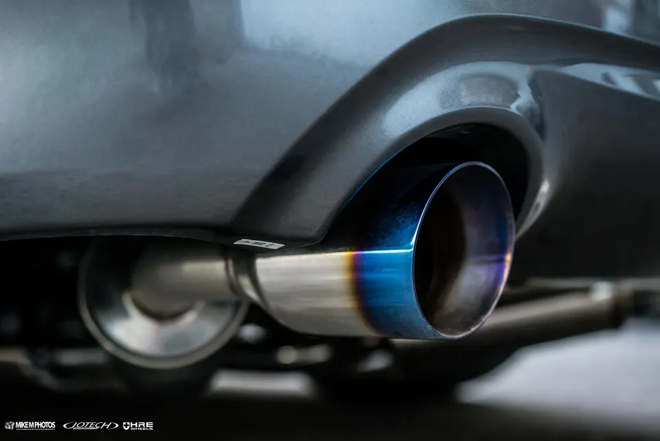 Close-up of a car's aftermarket exhaust tip with a burnt titanium finish, showing the rear bumper.