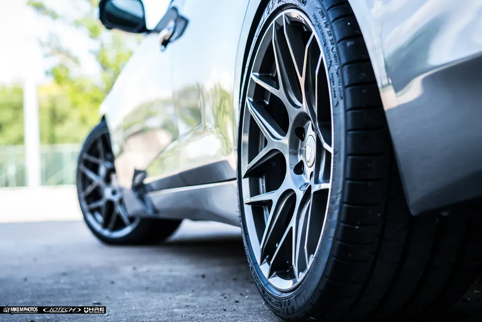 Close-up low angle shot of a custom multi-spoke wheel and performance tire on a silver sports car