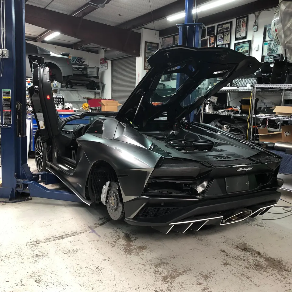 Lamborghini Aventador on a lift in a performance shop undergoing maintenance or modification, with wheels removed and engine bay open.