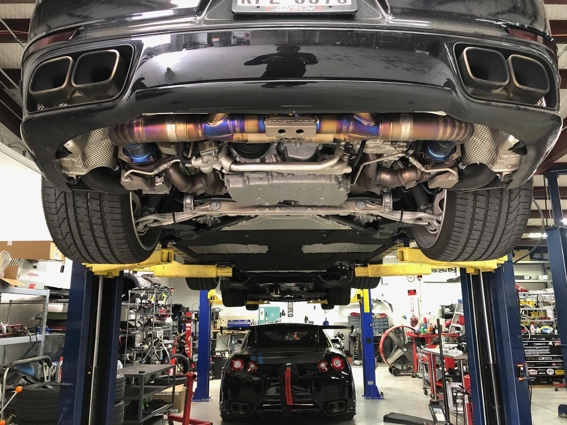 Underside view of a Porsche on a lift in a performance shop, showcasing a custom titanium exhaust system.