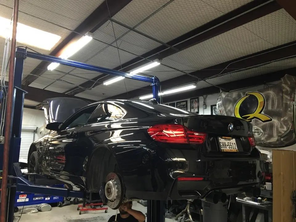 A black BMW M4 on a lift in a performance shop, with wheels removed and exhaust visible.