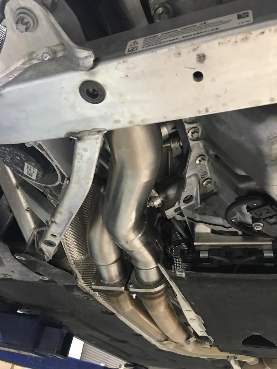 Close-up of a stainless steel performance exhaust system, including headers and downpipes, installed on the underside of a car.