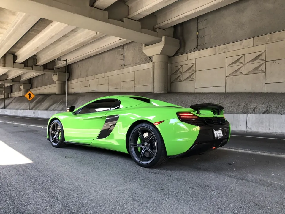 Bright green McLaren MP4-12C supercar parked under a concrete overpass, showcasing its sleek design and rear spoiler.