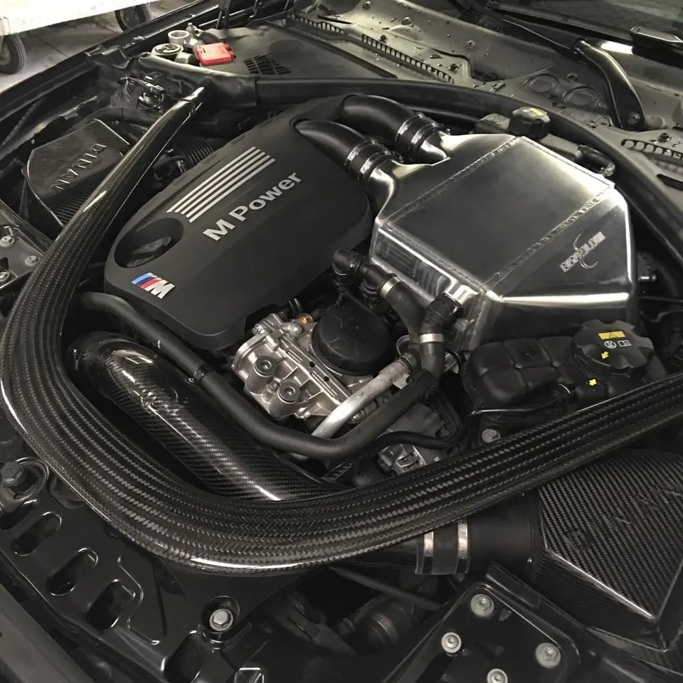 Detailed view of a BMW M Power engine bay featuring a carbon fiber intake system and an aftermarket intercooler.