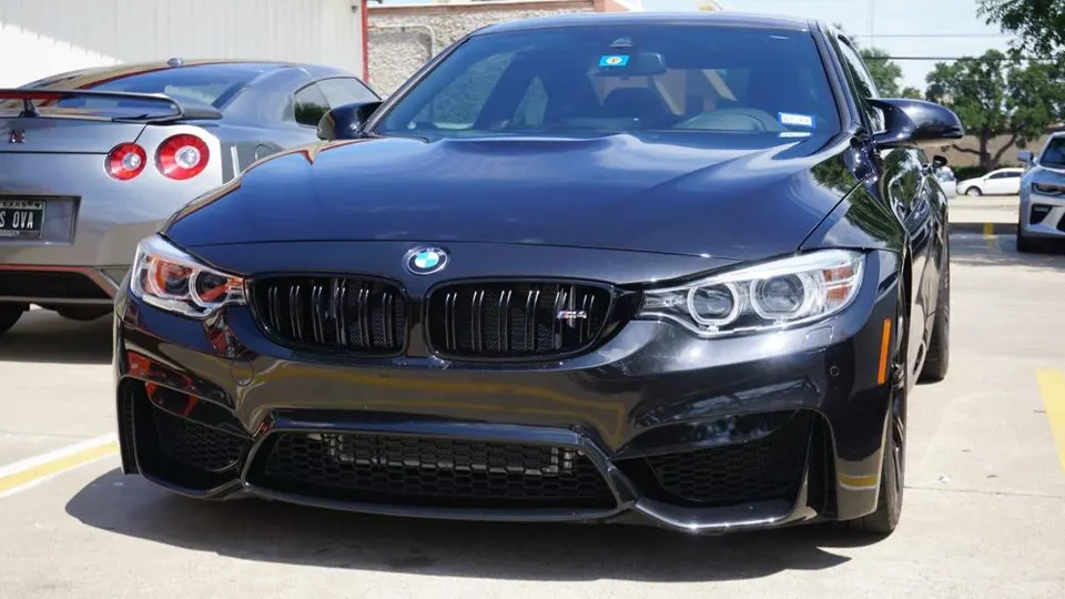 Black BMW M4 parked in front of a silver Nissan GT-R in a sunny outdoor setting, showcasing both vehicles.