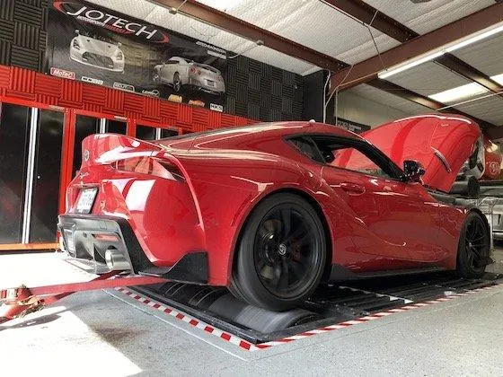 Red Toyota Supra on a dynamometer at Jotech Motorsports for performance tuning and horsepower measurement.