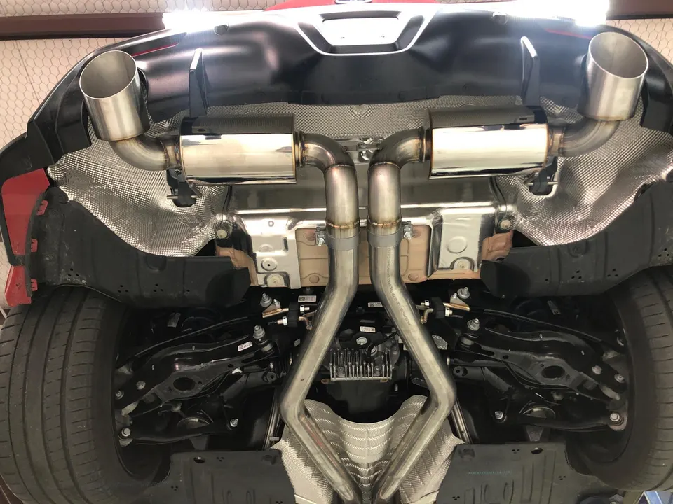 Underside view of a performance exhaust system installed on a sports car, featuring stainless steel piping and mufflers.