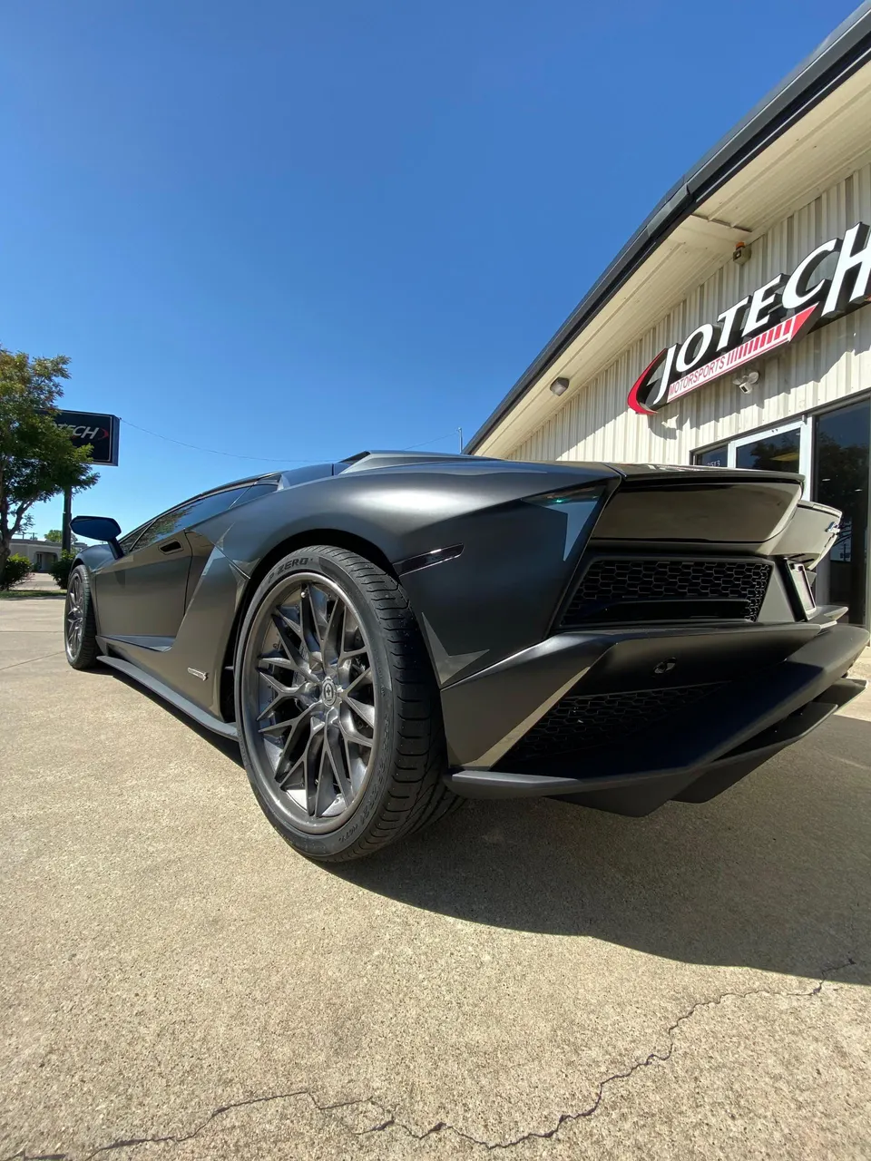 Matte black Lamborghini Aventador with custom HRE wheels and aggressive rear diffuser parked outside Jotech Motorsports.