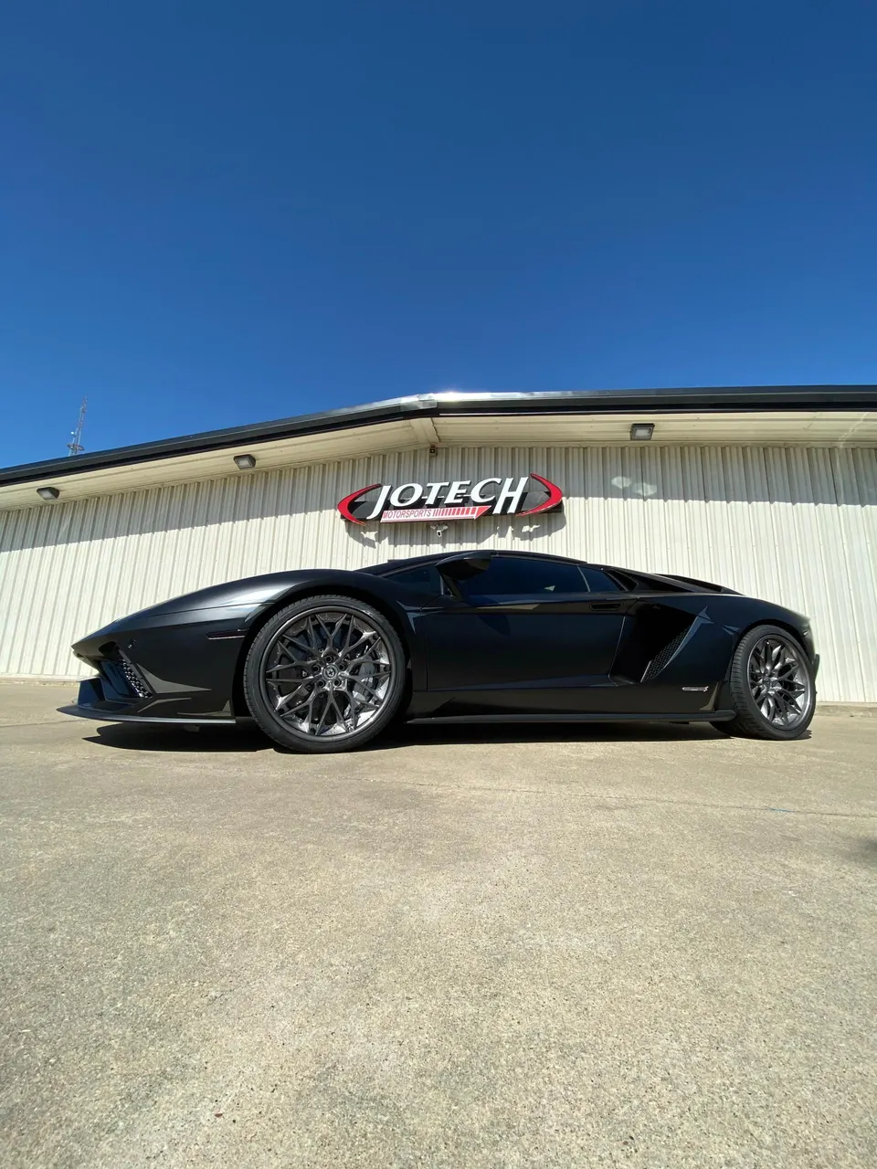 A black Lamborghini Aventador with aftermarket wheels parked outside Jotech Motorsports.