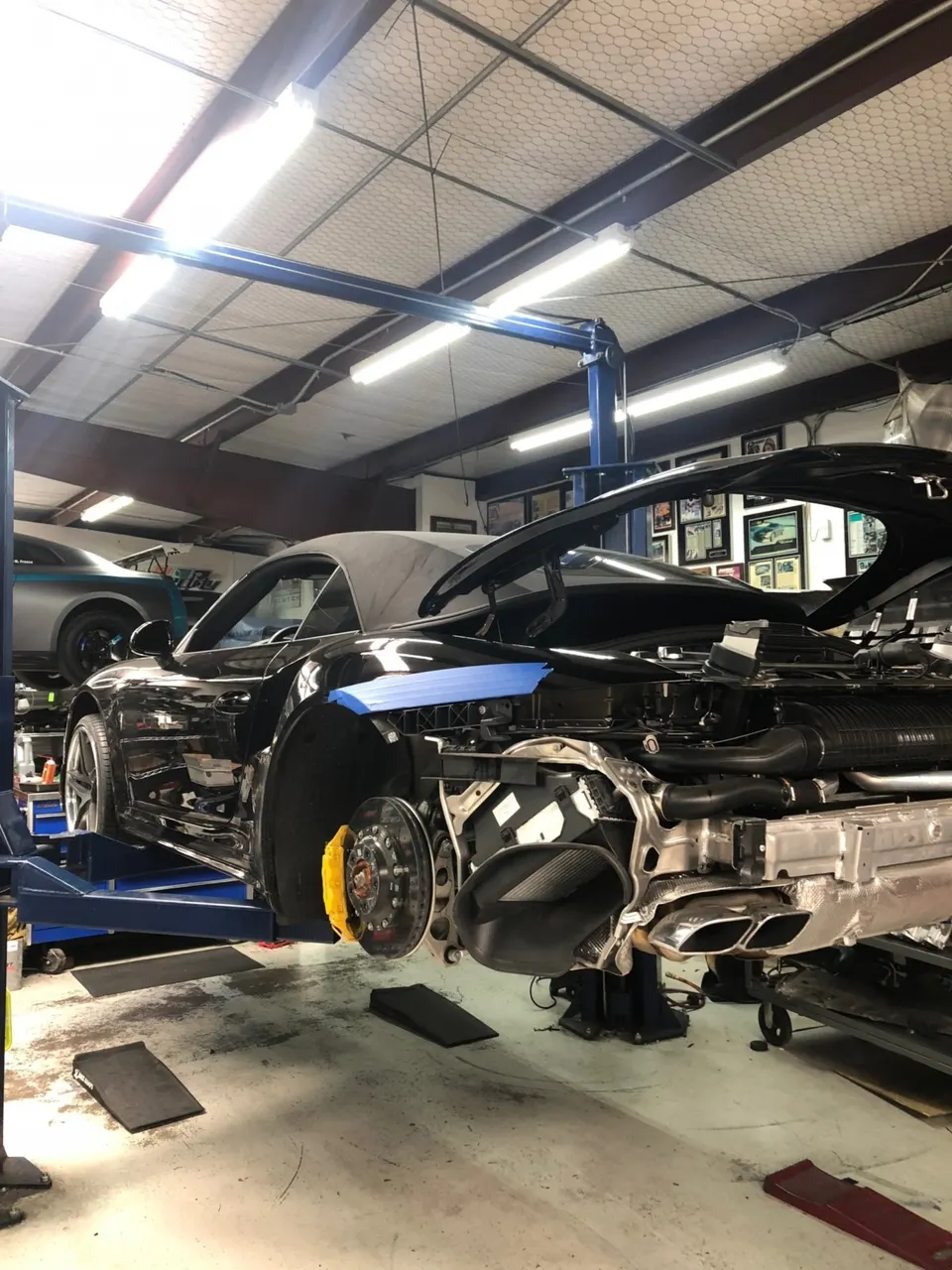 A McLaren supercar on a lift in a shop with its rear bumper removed, exposing the exhaust system and yellow brake calipers.