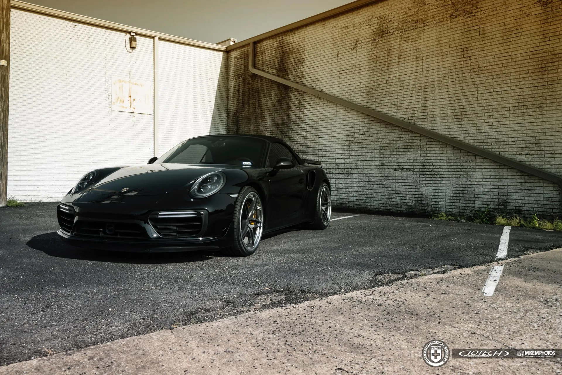 A sleek black Porsche 911 Turbo S parked in an urban setting, showcasing its aftermarket wheels and clean lines.