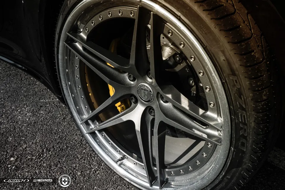 Close-up of a black car's custom HRE wheel with yellow brake calipers and Pirelli P Zero tire on asphalt.
