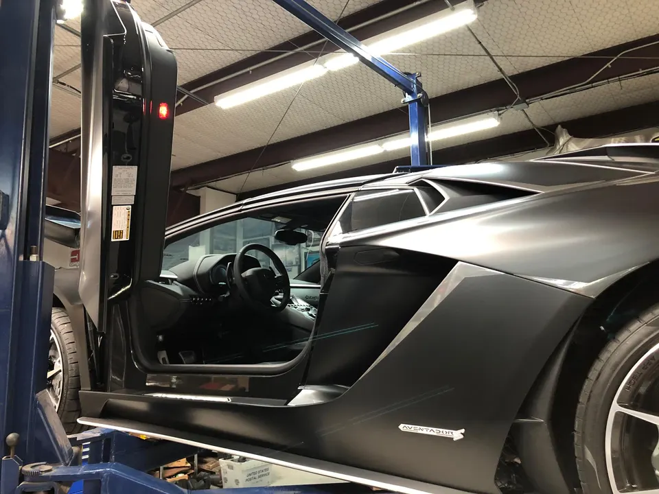 Matte black Lamborghini Aventador on a lift in a performance tuning shop with its scissor door open.