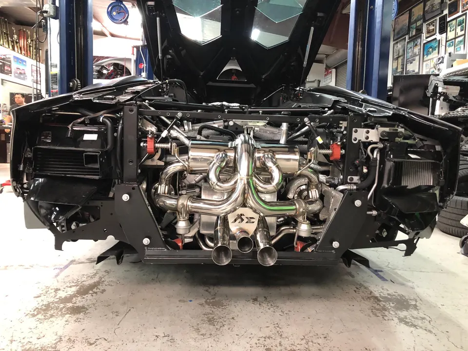 Rear view of a black Lamborghini Aventador in a shop, with its aftermarket performance exhaust system and engine exposed.