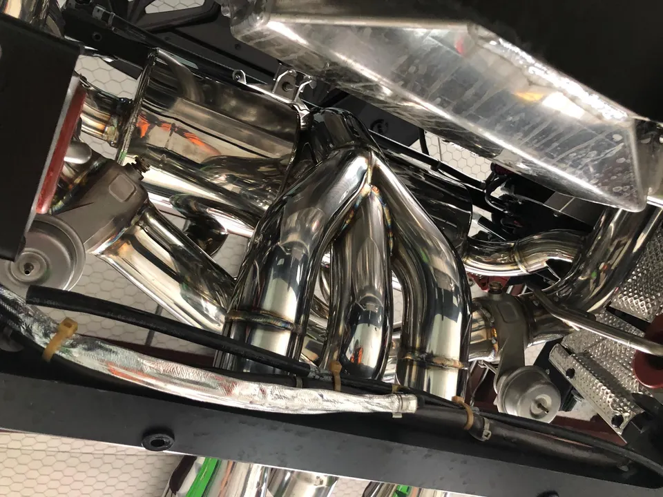 Close-up view of a high-performance stainless steel exhaust header and piping installed on a vehicle.
