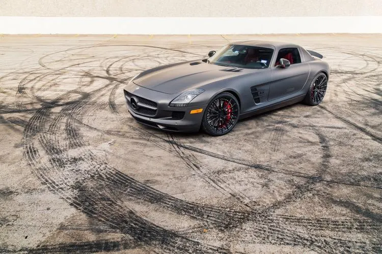 Matte grey Mercedes-Benz SLS AMG with custom black wheels and red calipers on an asphalt lot with tire marks.
