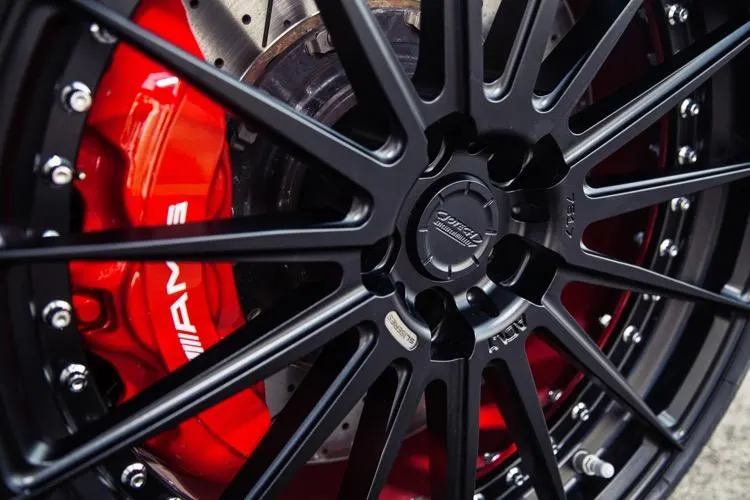 A close-up of a black ADV.1 wheel with a red AMG brake caliper and drilled rotor.
