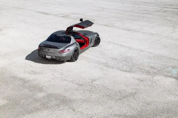 Overhead view of a grey Mercedes-Benz SLS AMG with red interior and open gullwing doors parked on a concrete surface.