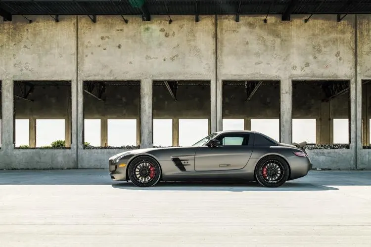Grey Mercedes-Benz SLS AMG with custom black wheels and red brake calipers parked in front of a concrete building.