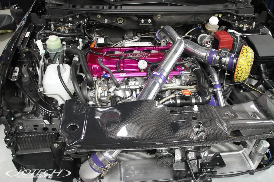 Detailed view of a modified engine bay featuring a pink valve cover, carbon fiber shroud, and HKS intake and boost piping.