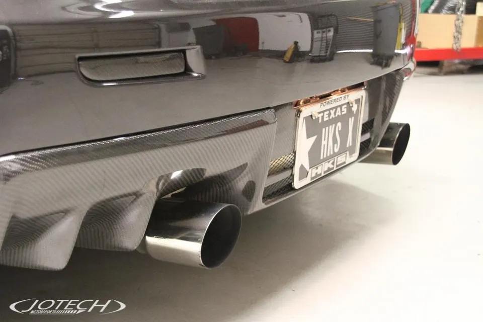 Rear view of a car showcasing a carbon fiber diffuser and aftermarket exhaust tips, with a Texas HKS license plate.