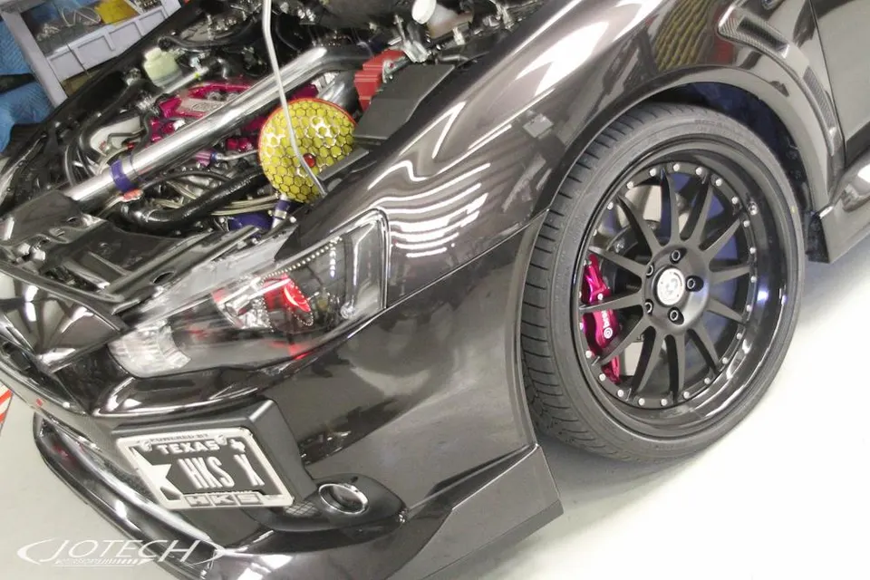 Close-up of a modified Mitsubishi Evo X with an open hood revealing a performance cold air intake, aftermarket wheels, and Brembo brakes.