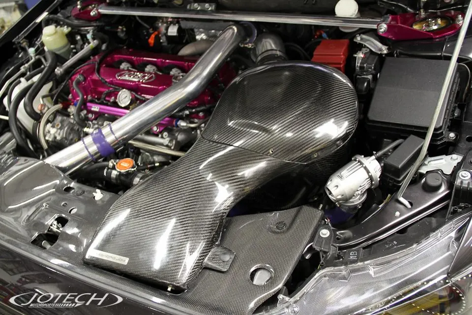 Close-up view of a highly modified engine bay featuring a large carbon fiber intake, custom pink valve cover, and blow-off valve.