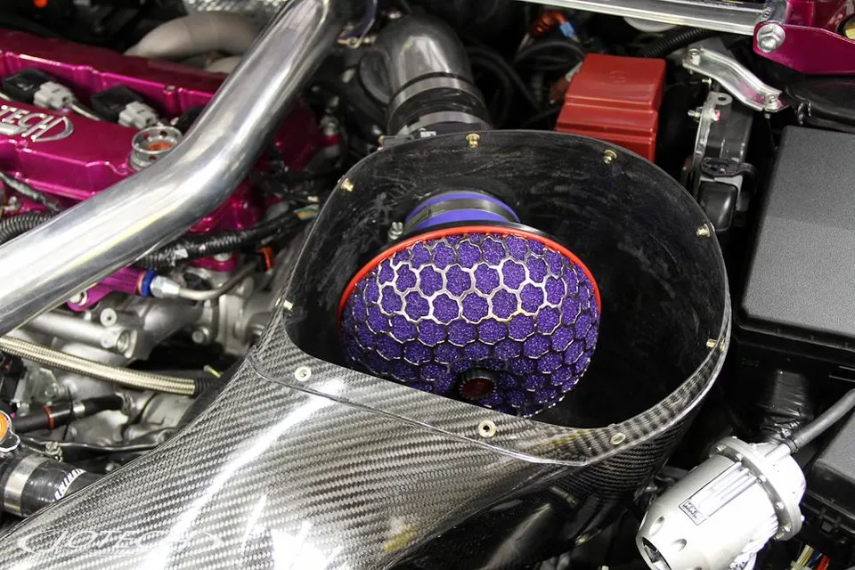 A close-up of a custom engine bay featuring a purple HKS air filter in a carbon fiber intake system.