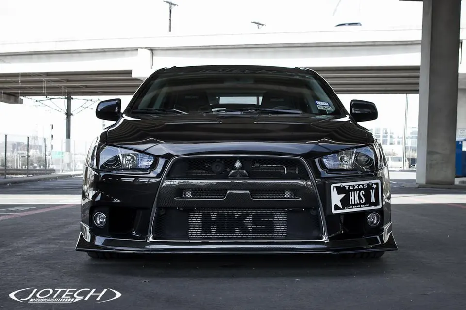 Front view of a black Mitsubishi Lancer Evolution X with a prominent HKS intercooler and carbon fiber aero.
