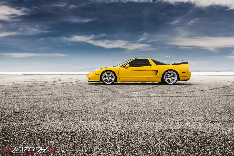 Yellow Honda NSX sports car with aftermarket wheels parked on a salt flat under a dramatic sky.