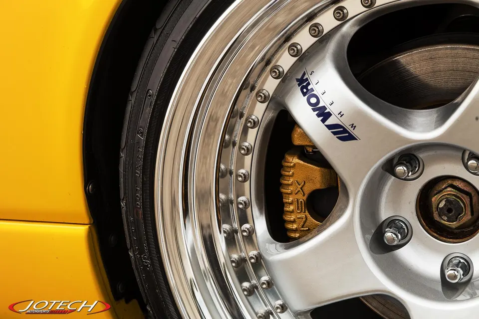 A close-up detail shot of a yellow car's Work Wheels, tire, and gold NSX brake caliper.