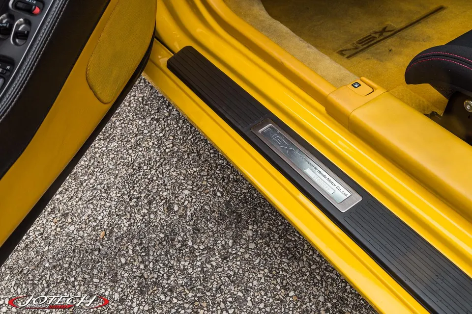 A close-up of the yellow interior and door sill of a Honda NSX, featuring the NSX logo on the sill plate.