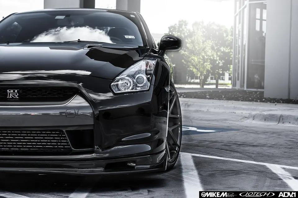 A black Nissan GT-R with ADV.1 wheels and a carbon fiber front lip, parked outdoors.