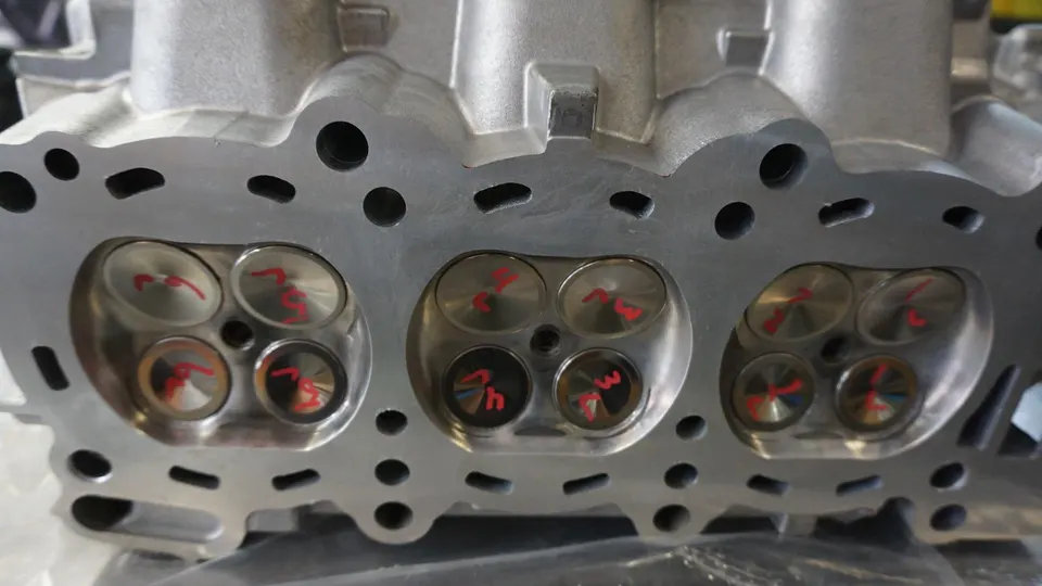 Close-up view of a machined engine cylinder head with visible valves, marked with red numbers.