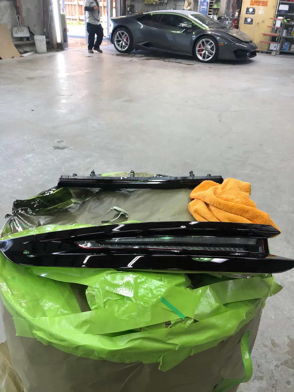 Lamborghini Huracan in a shop with a taillight assembly on a table, likely undergoing repair or customization.