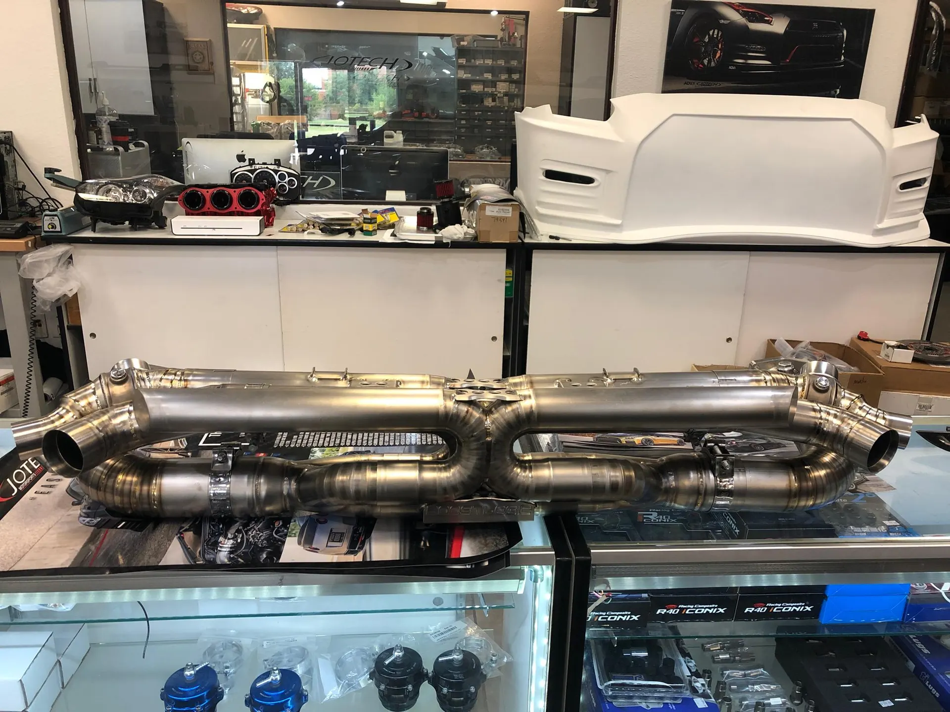 A titanium exhaust system and other performance car parts displayed in a Jotech Motorsports tuning shop.