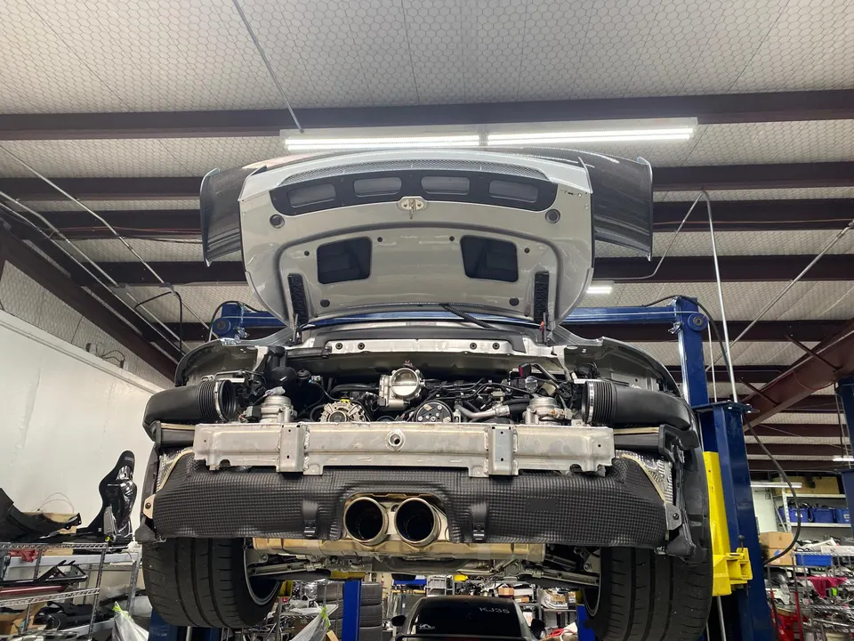 Rear view of a McLaren on a lift in a shop with the engine bay open, showcasing the exhaust system.