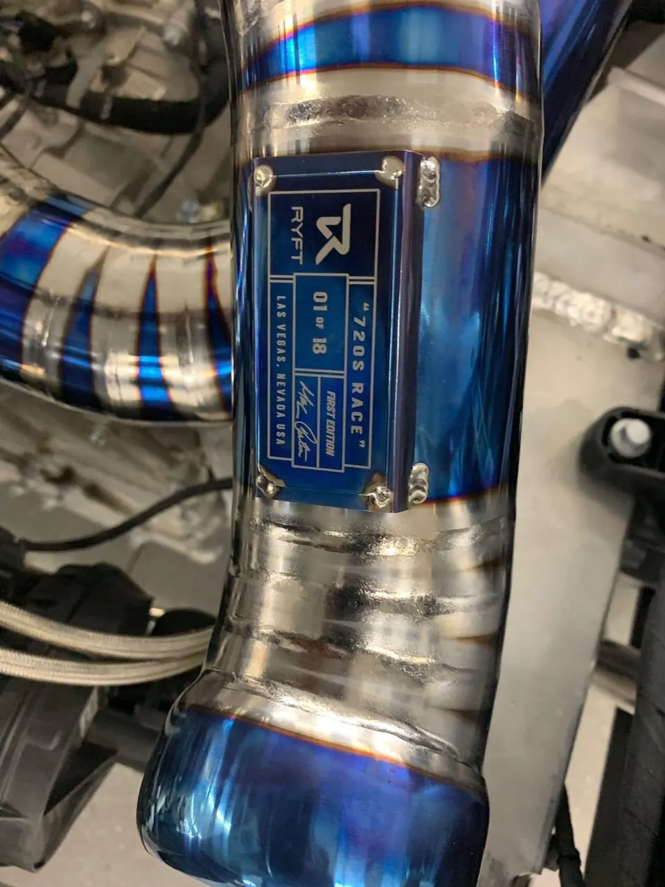 Close-up of a Ryft titanium exhaust pipe for a McLaren 720S Race, showing blue heat coloring and welds.