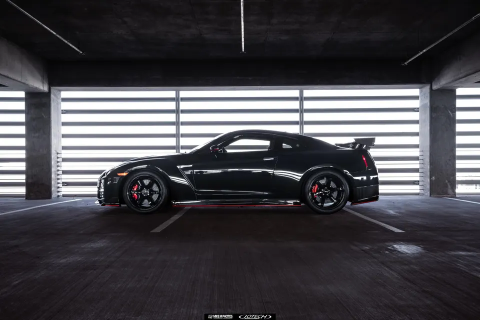 Black Nissan GT-R R35 with aftermarket wheels and red brake calipers parked in a modern parking garage.