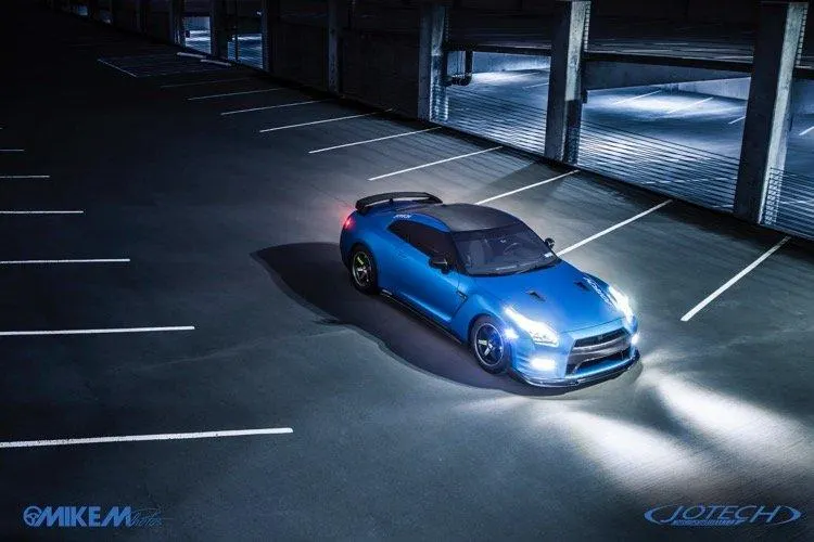 Blue Nissan GT-R with headlights on, parked in a dimly lit concrete parking garage at night.