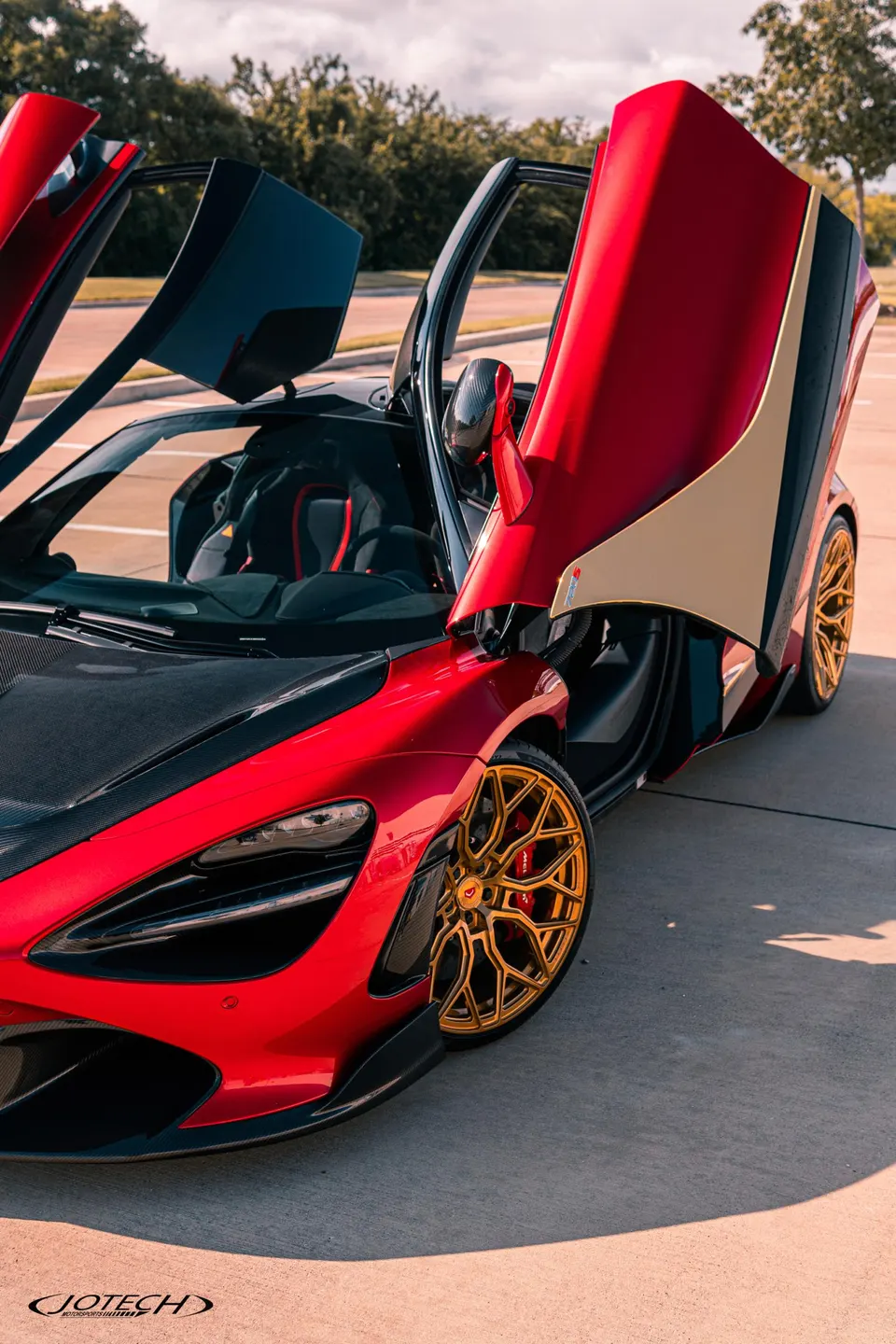 A red McLaren 720S with gold custom wheels and carbon fiber accents, parked outdoors with its butterfly doors open.