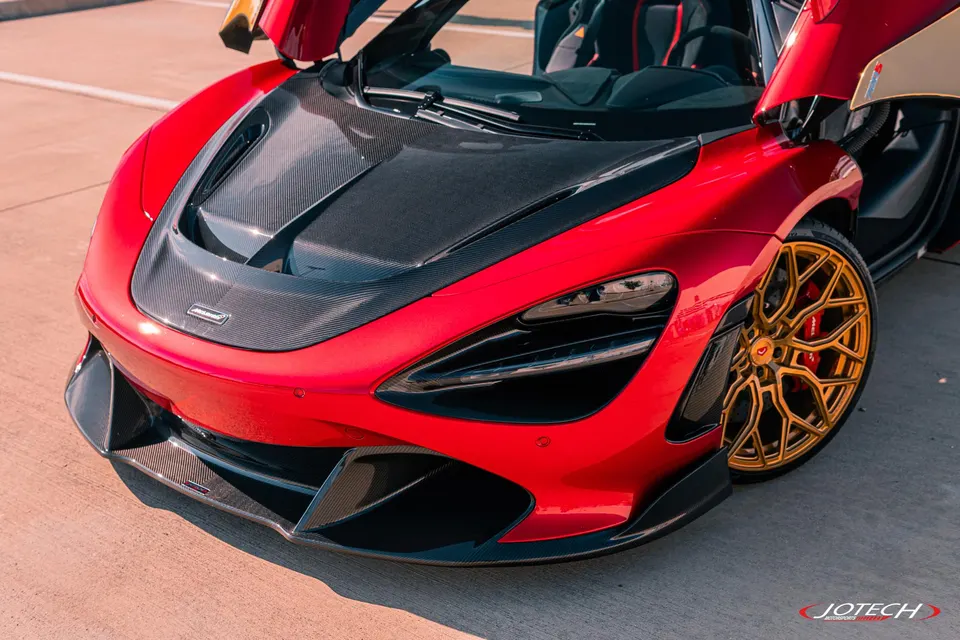 Red McLaren 720S with carbon fiber hood, front bumper, and gold custom wheels, parked outdoors.
