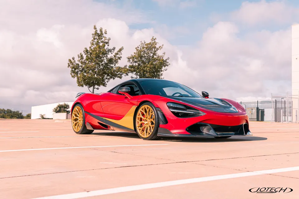 Red McLaren 720S with custom gold multi-spoke wheels parked outdoors under a cloudy sky.