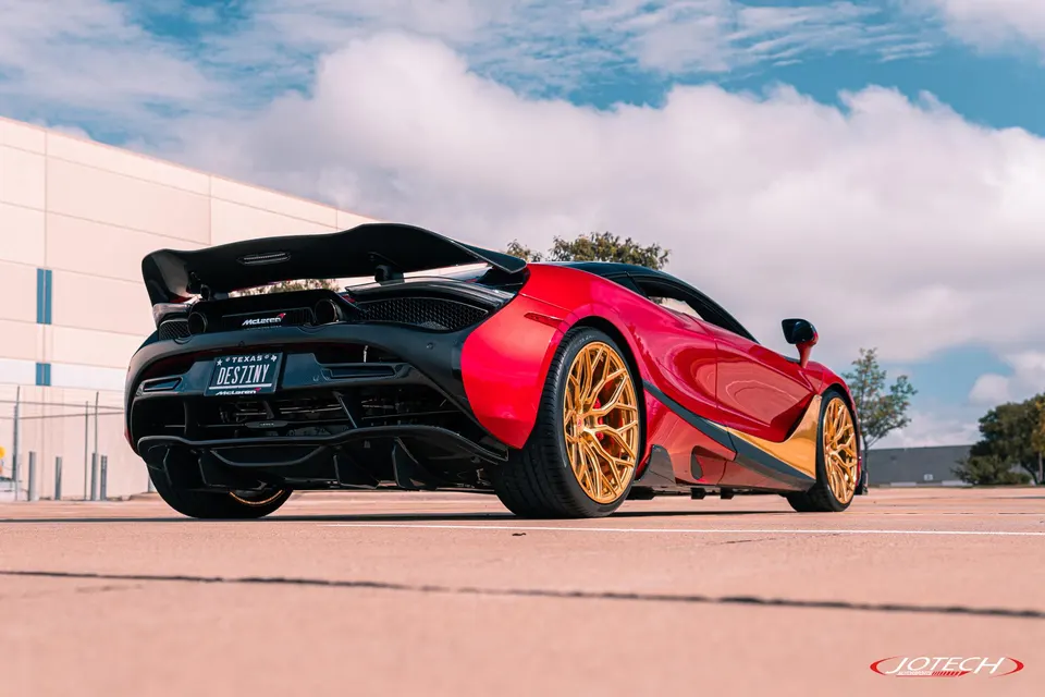 A red McLaren 720S with gold aftermarket wheels and a large carbon fiber rear wing parked outdoors.