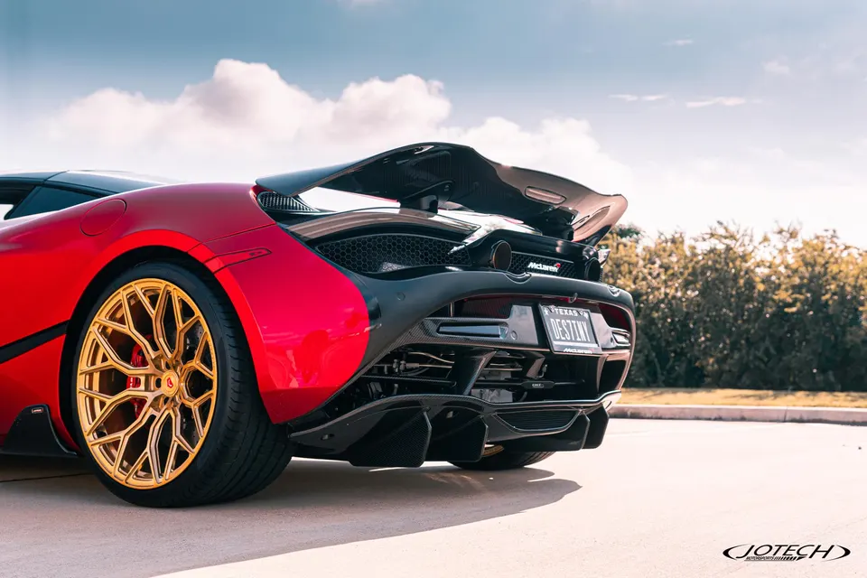 Rear view of a red McLaren 720S with custom gold wheels, carbon fiber wing, and diffuser parked outdoors.