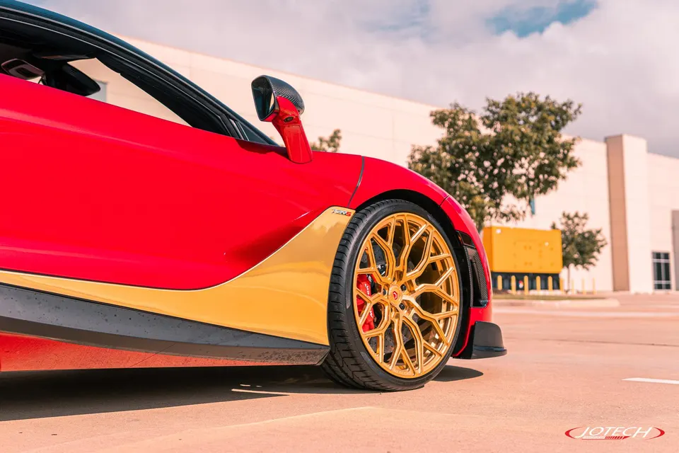 A red McLaren sports car with custom gold wheels and red brake calipers, parked outdoors.