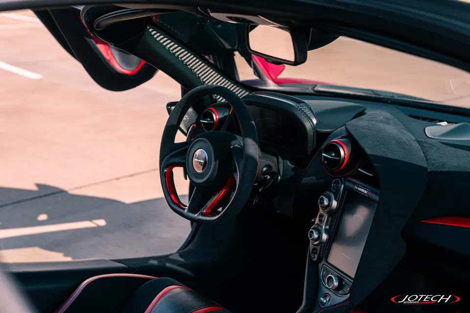 A detailed view of a McLaren's interior, showcasing the steering wheel, dashboard, and center console with red accents.