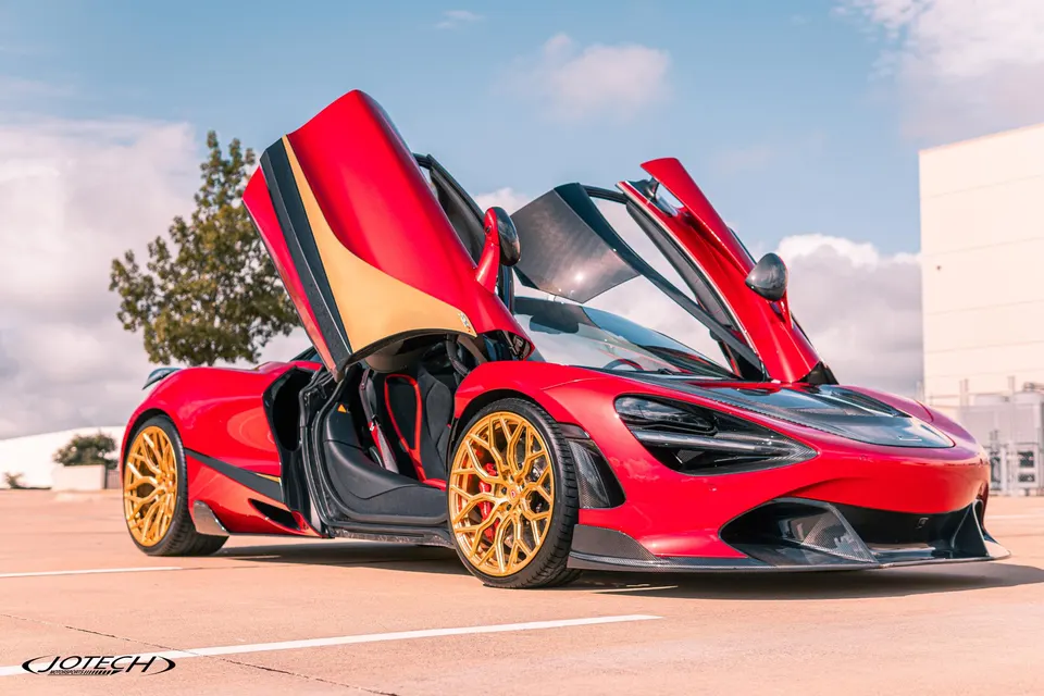 Red McLaren 720S with gold aftermarket wheels and carbon fiber aerodynamic parts parked outdoors under a blue sky.